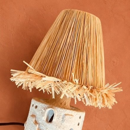 Raffia lamp shade on a ceramic base against a terracotta wall